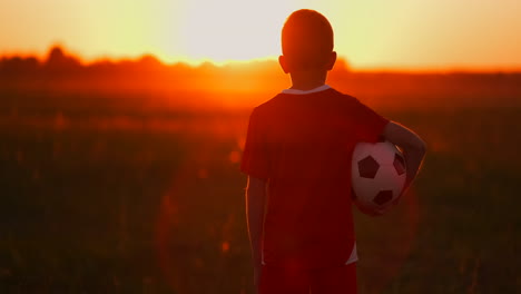 Junge-Mit-Einem-Ball-Auf-Einem-Feld-Bei-Sonnenuntergang.-Junge-Träumt-Davon,-Fußballspieler-Zu-Werden.-Junge-Geht-Bei-Sonnenuntergang-Mit-Dem-Ball-Auf-Das-Feld.